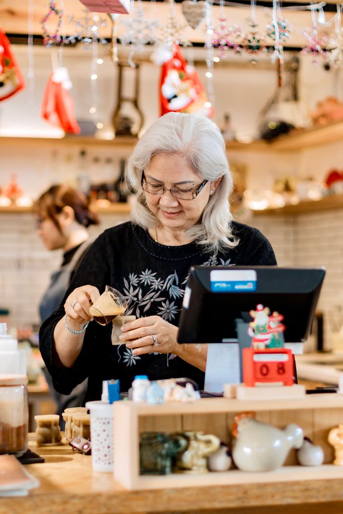Elderly woman in a café prepping a drink during holiday season. Cozy and festive.
