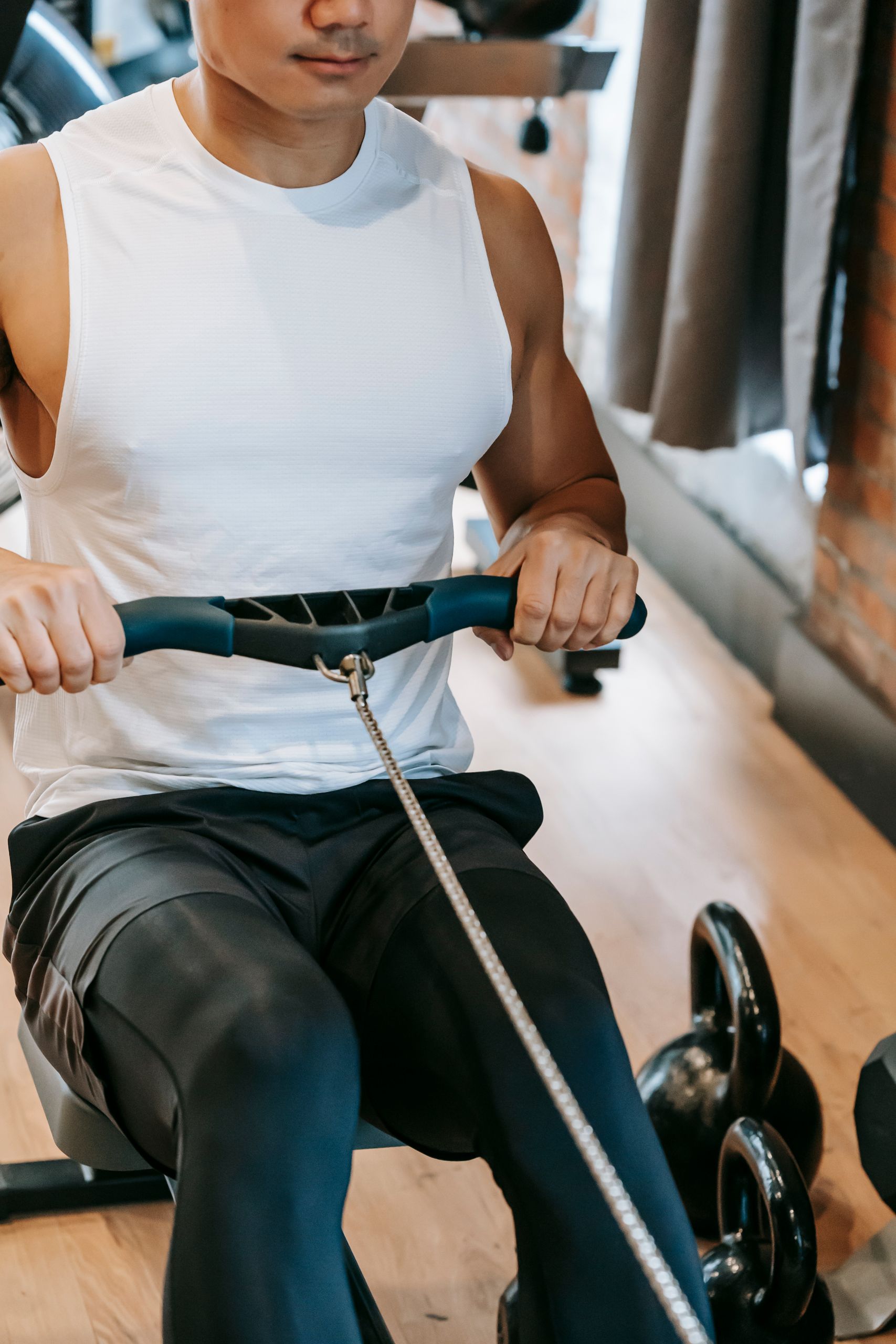 High angle of crop focused strong male athlete in sportswear doing exercise on rowing machine during training