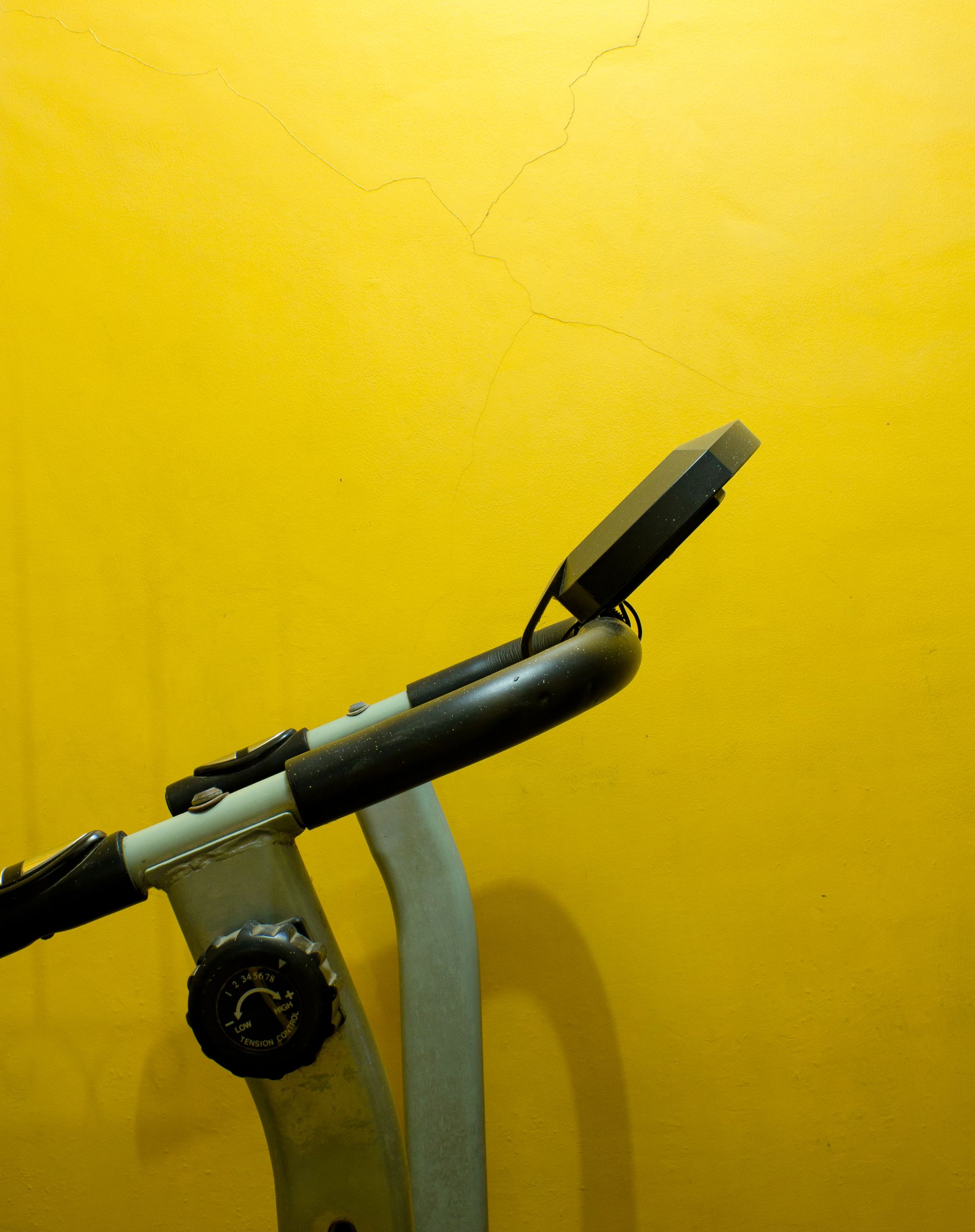 Minimalist shot of an exercise bike handlebar set against a bright yellow wall, creating a vibrant contrast.