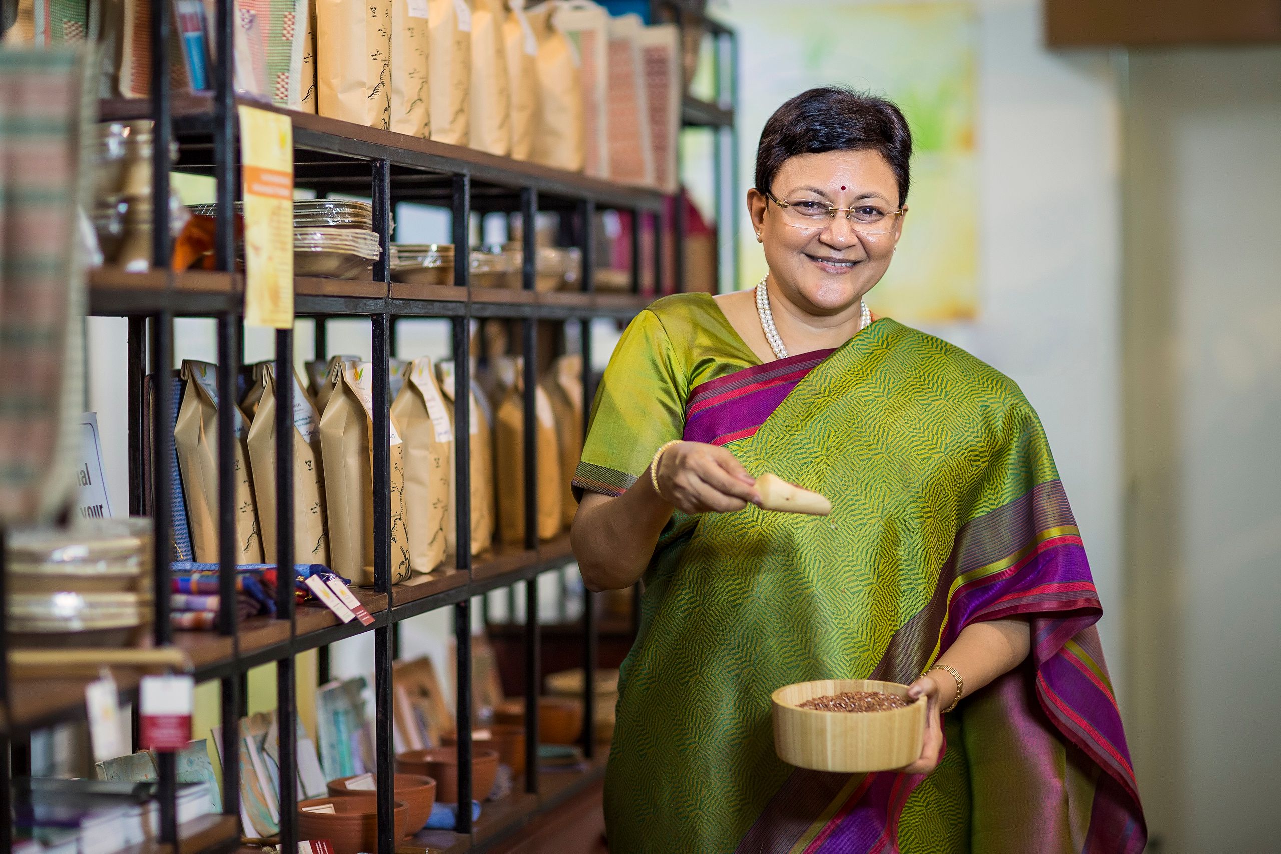 South Asian woman wearing sari smiling and working in an indoor store setting with shelves stocked.